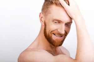 sintiéndose seguro de sí mismo. primer plano de un hombre barbudo ajustando su cabello y sonriendo mientras está de pie contra el fondo blanco foto