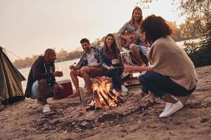 Life is awesome. Group of young people in casual wear smiling while enjoying beach party near the campfire photo