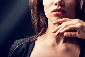 Pure beauty. Close-up of young woman holding hand near her chin while standing against black background photo