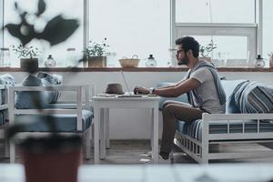 Full concentration at work. Serious young modern man in eyewear using computer while sitting on the sofa photo
