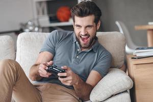 That is my best round Excited young handsome man playing video game and keeping mouth open while sitting on the couch at home photo