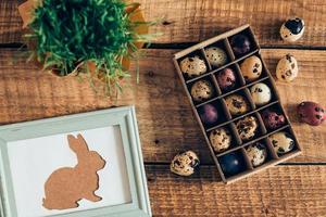Spring holidays. Top view of Easter bunny in picture frame and box of Easter quail eggs lying on wooden rustic table photo