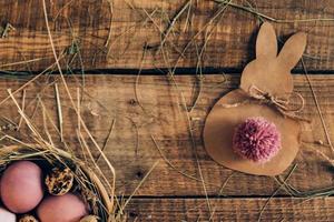 Ester Bunny. Top view of colored Easter eggs in bowl with hay and Easter bunny made from brown paper lying on wooden rustic table photo