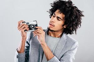 Can this thing make selfie Handsome young African man holding retro styled camera and looking at it while standing against grey background photo