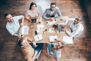 Best team ever Top view of group of six people looking at camera with smile while sitting at the office table photo