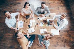 Best team ever Top view of group of six people looking at camera with smile while sitting at the office table photo