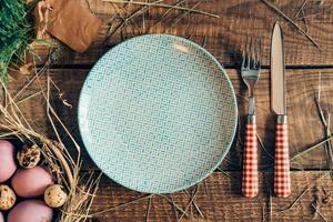 Easter dinner. Top view of Easter eggs in bowl and plate with fork and knife lying on wooden rustic table with hay photo