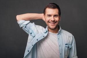 su sonrisa es increíble, un joven alegre que mira la cámara con una sonrisa mientras se enfrenta a un fondo gris foto