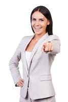 I choose you Happy young businesswoman in suit pointing you and smiling while standing against white background photo