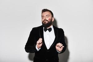 Handsome young man in full suit keeping eyes closed and gesturing while standing against grey background photo