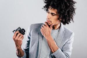 How does this thing works Handsome young African man holding retro styled camera and looking at it while standing against grey background photo