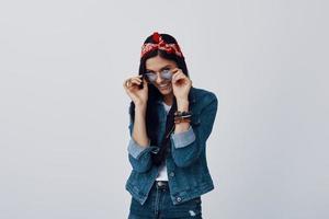 Attractive young woman in bandana adjusting eyewear and smiling while standing against grey background photo