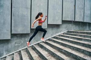 Full length of young woman in sports clothing jogging while exercising on the steps outdoors photo