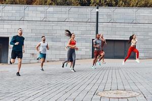 toda la longitud de los jóvenes en ropa deportiva trotando mientras hacen ejercicio al aire libre foto