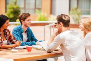 Enjoying studying together. Group of happy young people smiling and discussing something while sitting at the wooden desk outdoors photo