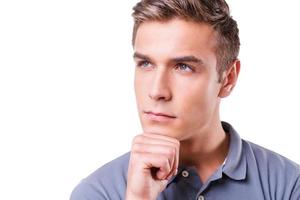 Handsome day dreamer. Thoughtful young man holding hand on chin and looking away while standing isolated on white background photo