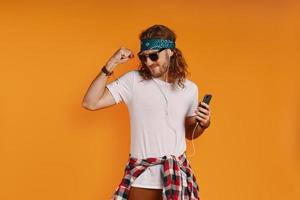 Playful young man listening music and smiling while standing against yellow background photo