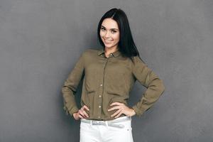 sentirse bien y verse bien. mujer joven feliz con ropa informal elegante parada en un fondo gris y tomándose de la mano en la cadera foto