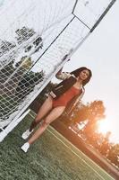 Listo para jugar. toda la longitud de una joven atractiva en bikini rojo posando cerca del poste de gol en el campo de fútbol foto