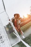 hermoso futbolista. toda la longitud de una joven atractiva en bikini rojo posando cerca del poste de gol en el campo de fútbol foto