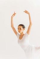 Dancing with passion. Beautiful young ballerina in white tutu keeping arms raised while dancing against white background photo