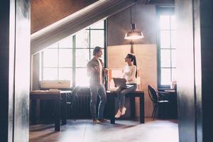 Nice talk with colleague. Cheerful young man and woman discussing something and smiling during their coffee break in creative office photo