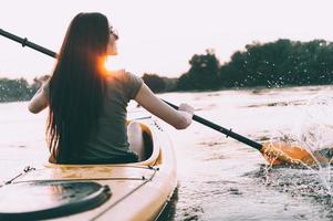 Enjoying perfect sunset on river. Rear view of beautiful young woman kayaking on river and with sunset in the background photo