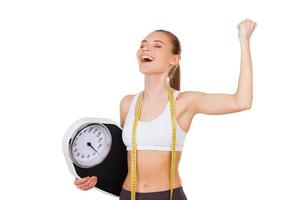 Worked off her excess weight. Happy young woman in sports clothing holding weight scale and gesturing while standing isolated on white photo