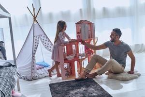 Carefree time together. Father and daughter playing with a dollhouse together while sitting on the floor in bedroom photo