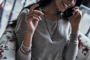 Pleasant talk. Close-up of young woman playing with her necklace and smiling while talking on the smart phone photo