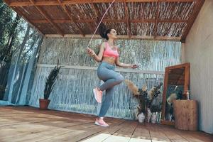 toda la longitud de una hermosa joven con ropa deportiva usando una cuerda para saltar en el patio foto