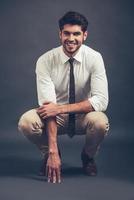 Can you resist his smile Full length of confident young handsome man looking at camera with smile while sitting crouched against grey background photo