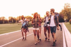 hermoso día para caminar. grupo de jóvenes con mochilas caminando juntos por la carretera y luciendo felices foto