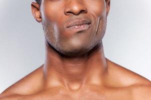 Feeling doubt. Cropped image of young African man grimacing while standing against grey background photo