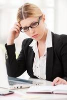 Thinking about solutions. Thoughtful mature woman in formalwear holding head in hand while sitting at her working place photo