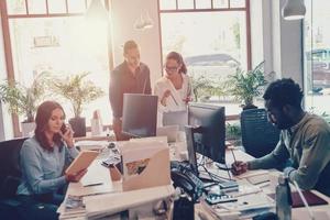 grupo de jóvenes modernos con ropa informal inteligente que se comunican y usan tecnologías modernas mientras trabajan en la oficina foto