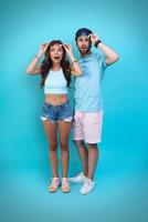 Full length of surprised young couple looking at camera while standing against blue background photo