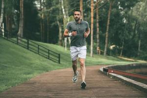 comenzando el día desde el trote matutino. toda la longitud de un joven apuesto con ropa deportiva trotando en el parque foto