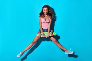 Mid-air fun. Full length of playful young woman smiling and looking at camera while hovering against blue background photo