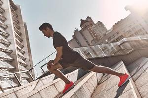 On the way to great shape. Young man in sports clothing warming up while exercising on the stairs outdoors photo