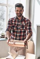 con amor para ti. apuesto joven dando una caja de regalo y mirando a la cámara con una sonrisa mientras está de pie en el espacio de trabajo creativo foto