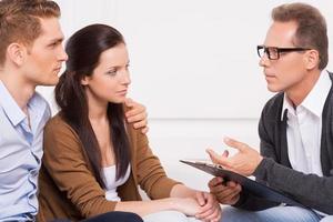 Consulting with family psychiatrist. Beautiful young couple listening to the psychiatrist telling something and gesturing photo