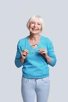 Fashionable senior female. Beautiful senior woman looking at camera and smiling while standing against grey background photo