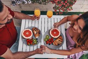 Top view of loving young couple in casual holding hands and smiling while having breakfast photo