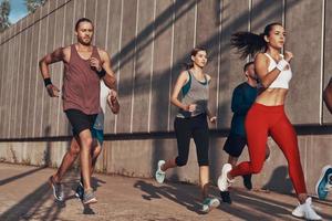 toda la longitud de la gente con ropa deportiva trotando mientras hace ejercicio en la acera al aire libre foto