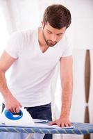 Ironing shirt. Confident young man ironing shirt on ironing board at home photo