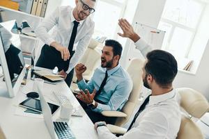 Big success. Group of young modern men in formalwear smiling while working in the office photo