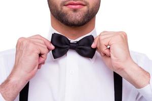 Man adjusting bow tie. Close-up of young man in white shirt adjusting his bow tie while standing isolated on white photo