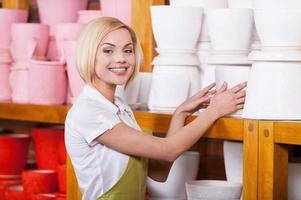 Selling the best flower pots. Beautiful young blond hair woman in apron adjusting flower pots in the gardening store photo