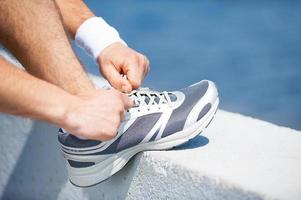 Tying shoelaces. Close-up of man tying shoelaces on sports shoe while standing outdoors photo